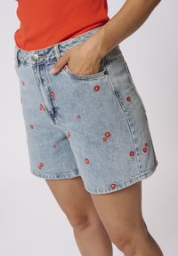 Sinised teks shorts, millel on punased lille tikandid, viis taskut ja tavaline vöökohaga, valmistatud puuvillast.