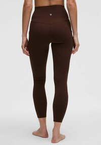 Pruunid kõrge talje leggingsid, millel on sujuv ja sile tekstuur. Omab vormitud disaini ja peeneid õmblusdetailide. Ei ole nähtavaid mustreid ega metallosade.