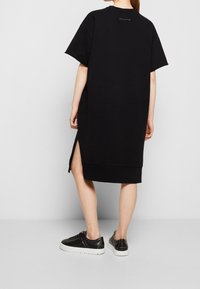 Vestido sudadera negro de corte grande con mangas cortas, abertura lateral, dobladillo acanalado, hecho de suave tela de algodón. Detalle del logo blanco en la parte posterior.