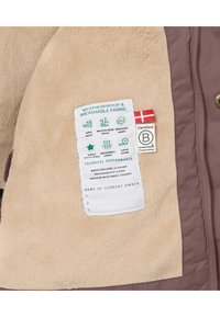 Braune und beige Jacke mit weichem Fleece-Innenfutter, ausgestattet mit einem Pflegeetikett mit wetterfesten Indikatoren und einer dänischen Flagge. Geklebte Nähte sichtbar.