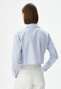 Maglietta a maniche lunghe blu chiaro e bianca a righe, con colletto classico e polsini con bottoni.