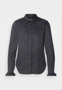 Blouse noire à manches longues avec boutons cachés sur le devant, col pointu et petites poignets à volants aux manches.