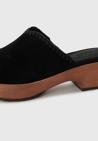 Sorte semskede tresko med avrundet åpen design, med en tre såle og dekorativ søm langs øvre kant. Strukturert finish.