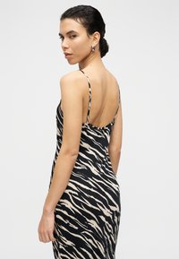 Μαύρο και μπεζ φόρεμα με ρίγες τίγρης, λεπτές τιράντες, χαμηλή πλάτη και εφαρμοστή σιλουέτα. Λείο ύφασμα με ελαφριά γυαλάδα.