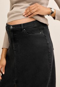 Minifalda de mezclilla negra con un diseño ajustado, bolsillos frontales y costuras en contraste. El material tiene una textura suave con un ligero brillo.
