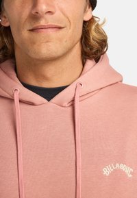 Pink hoodie made of soft fabric, featuring a drawstring hood and a curved white logo. Smooth texture with tonal color uniformity.