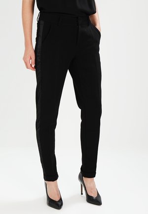 Pantalons fuselés noirs avec une finition en tissu lisse, présentant des panneaux latéraux en satin et deux poches avant, associés à des talons hauts noirs.