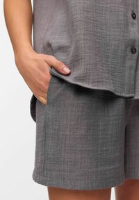 Pantalones cortos de lino grises con un ajuste relajado, que cuentan con un bolsillo lateral y un sutil patrón texturizado. Detalle de botón en la cintura.