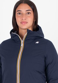 Giacca con cappuccio blu navy con zip frontale, caratterizzata da una striscia multi-colorata, logo sul petto e una texture liscia.