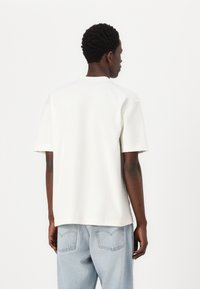 Camiseta de algodón blanca de manga corta con un corte holgado. Cuello redondo prensado y dobladillo recto, combinada con jeans de mezclilla azul claro.