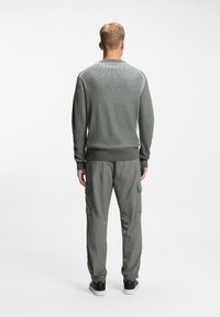 Πράσινο πλεκτό πουλόβερ με μακριά μανίκια και στρογγυλή λαιμόκοψη, σε συνδυασμό με ανοιχτό γκρι παντελόνι cargo με πλαϊνές τσέπες και ελαστικές μανσέτες.