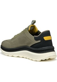 Zapatillas ligeras de color verde oliva con parte superior de malla y tacón negro. Presentan un acento amarillo cerca del tobillo y una suela blanca texturizada.