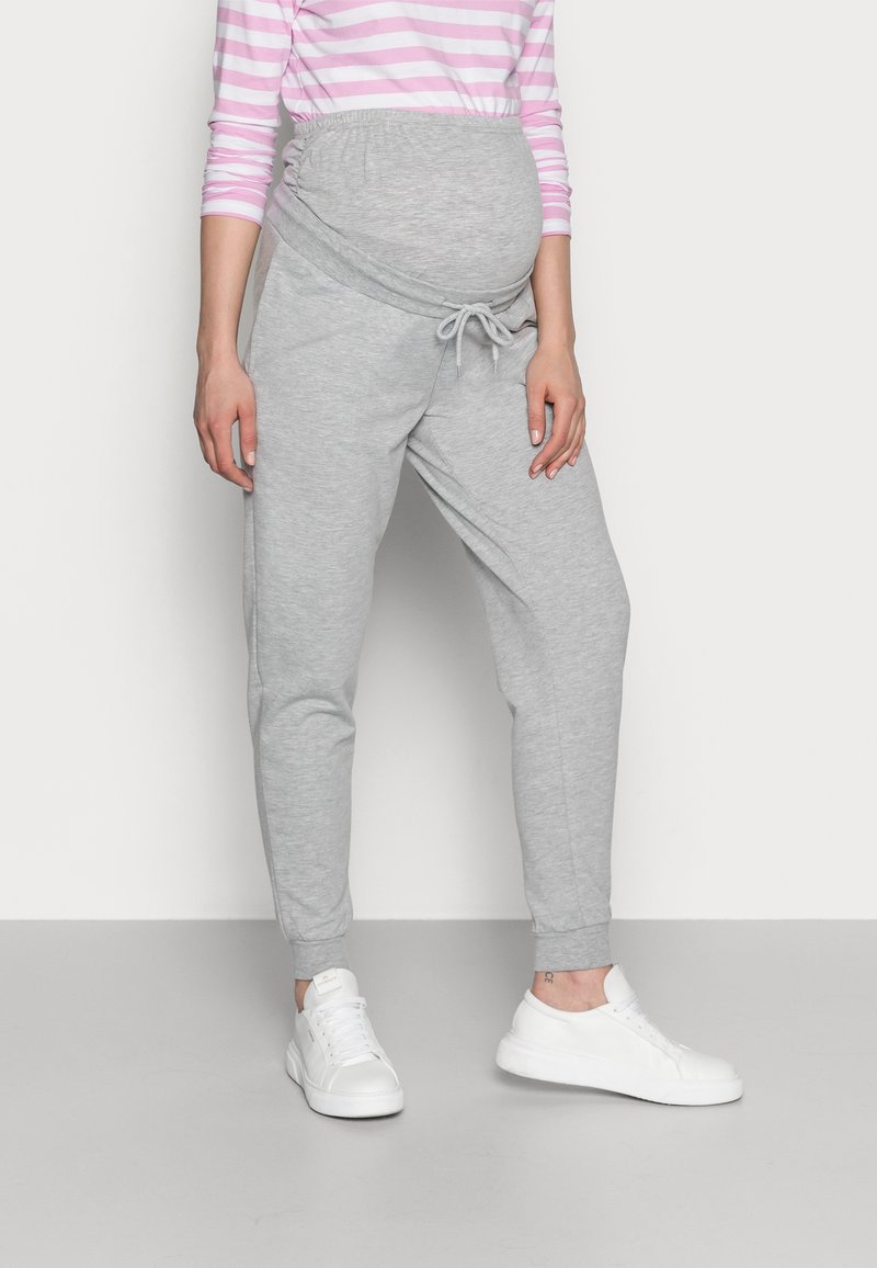 Grå gravide joggers med snor i livet, smalnede ben og elastiske mansjetter. Kombinert med hvite joggesko og en rosa stripete langermet topp.