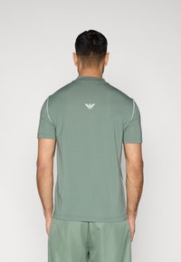 Πράσινο αθλητικό μπλουζάκι με κοντά μανίκια, κατασκευασμένο από διαπνέον ύφασμα. Διαθέτει διακριτικό λογότυπο στο πίσω μέρος και αντίθετες λευκές ραφές που προσθέτουν λεπτομέρειες.