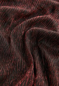 Black fabric with red shimmering threads, featuring a wave-like pattern and smooth texture, draped to show depth and movement.