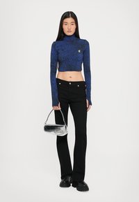 Royal blue cropped turtleneck sweater with a textured pattern, paired with black flared pants and a silver handbag with a curved shape.
