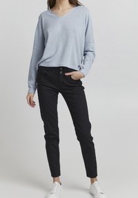 Lichtblauwe v-hals sweater met een gestructureerde brei, gecombineerd met zwarte slim-fit broek met een sluiting met twee knopen. Witte sneakers maken de look compleet.