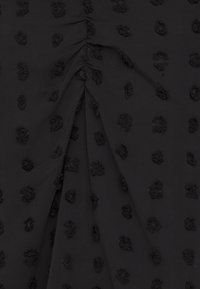 Tessuto nero con punti neri texture, caratterizzato da sezioni arruffate. La superficie è liscia con un design giocoso e in rilievo su tutta la superficie.