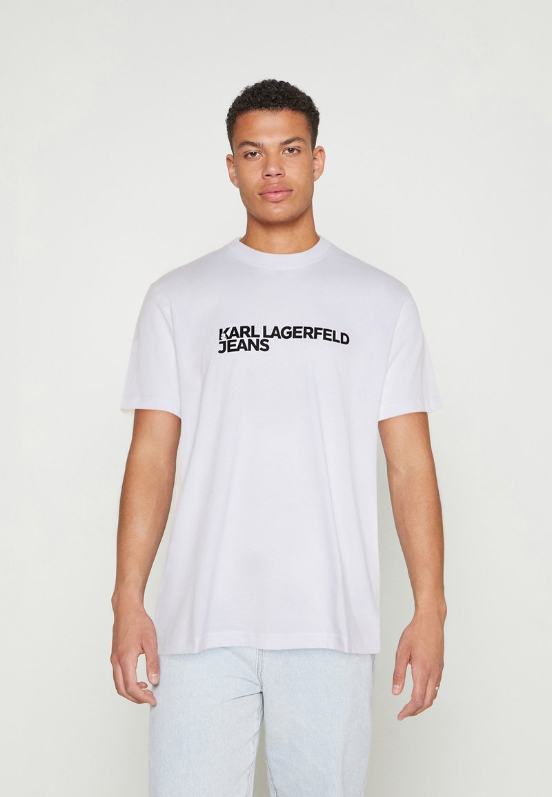 Valge puuvillane T-särk, millel on must trükitud logo "KARL LAGERFELD JEANS", mis on rinnal. Särgil on ümmargune kaelus ja lühikesed varrukad.
