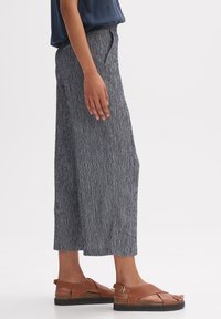 Bredbenta byxor i marinblått med ett strukturerat mönster, tillsammans med bruna lädersandaler som har ett rem- och spänndetalj.