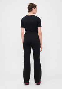 T-shirt ajusté noir à manches courtes associé à un pantalon évasé noir taille haute. La tenue présente un tissu lisse et une silhouette épurée.