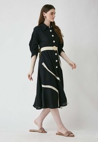 Marineblaues Hemdkleid mit cremefarbenen Streifen, tailliert mit einem runden Schnallen-Gürtel. Kurze Puffärmel und fließender Saum.