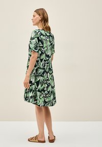 Sukienka z krótkim rękawem z ciemnozielonym tłem, na którym widnieją duże zielone i białe wzory liści. Długość do kolan z falbaną na końcu.