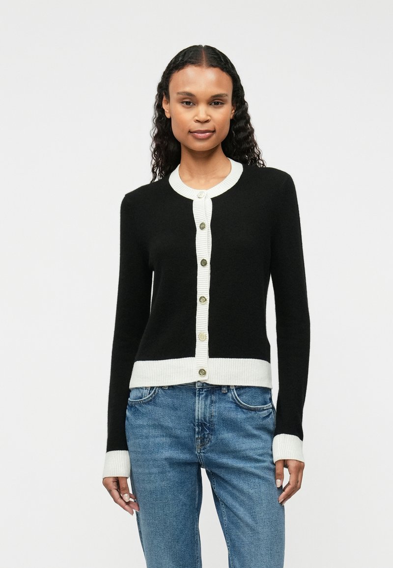 Cardigan noir avec un col et un ourlet côtelés blancs, comportant six boutons verts sur le devant. Texture douce et design ajusté.