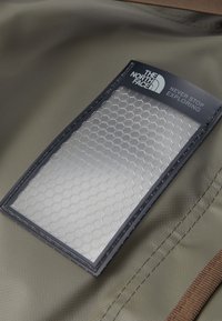 Green fabric with a textured finish features a hexagonal-patterned, clear pocket bordered by dark navy material and brown accents.