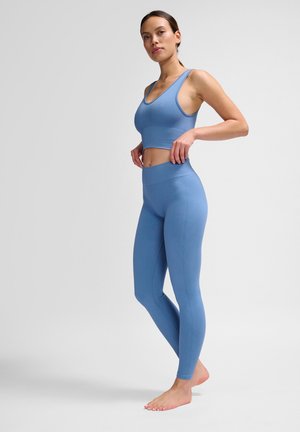 Blue ribbed sports bra and high-waisted leggings, featuring a fitted design and seamless texture. Minimalist style with a smooth finish.