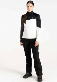 Langärmliges Oberteil in Weiß und Schwarz mit einem Reißverschlusskragen und einem farblich blockierten Design. Kombiniert mit schwarzen Hosen und robusten schwarzen Schuhen.