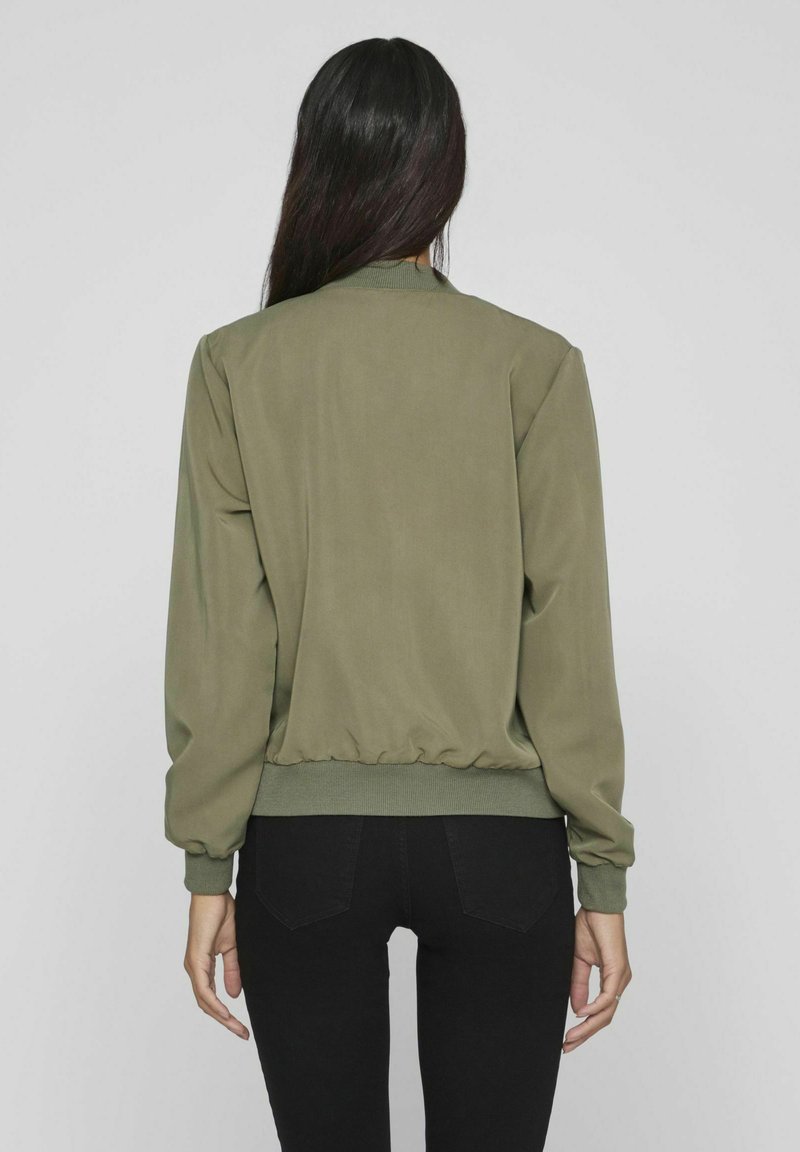 Olivgrüne Bomberjacke mit glatter Textur, gerippten Bündchen und Saum; von hinten sichtbar, kombiniert mit schwarzen Jeans.