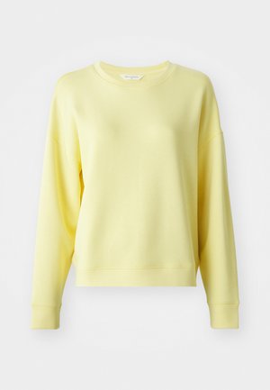 Sárga kapucnis pulóver kerek nyakkal, hosszú ujjal, ejtett vállakkal és puha textúrával. Enyhén laza szabású, bordás mandzsettával.