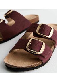 Burgundy sandaler med två breda remmar som har guldfärgade spännen, korkfot sula och mönstrad svart gummisula. Mjuk mockaliknande material.