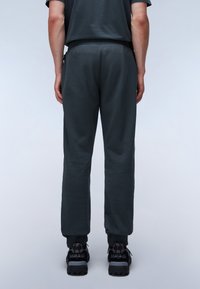 Donkergrijze sweatpants met een geribde tailleband en boorden, gemaakt van zachte stof. Gedragen met zwarte sportschoenen met accenten aan de zijkant.