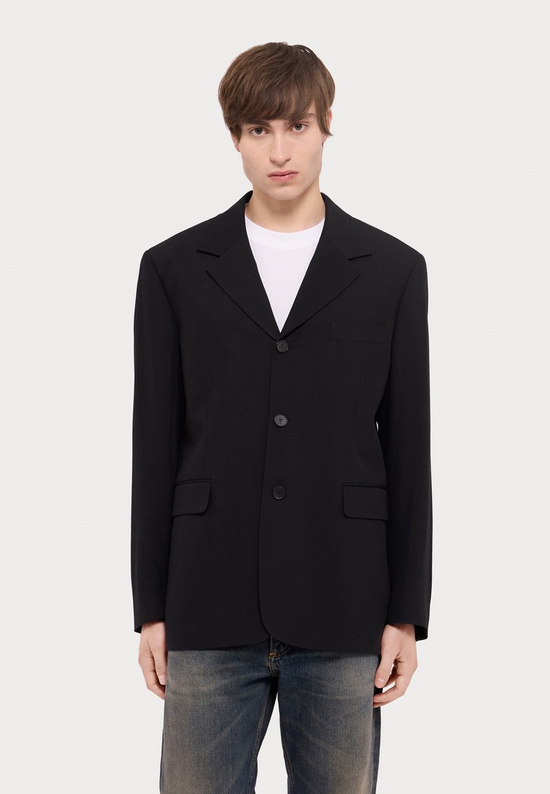 Schwarzer strukturierter Blazer mit Reverskragen, einer Brusttasche und zwei Fronttaschen. Knopfverschluss, lange Ärmel und mittelschwerer Stoff.