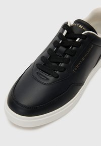Juodi odiniai sportbačiai su apvaliu pirštu, balta gumine padu, juodais raiščiais ir aukso spalvos "TOMMY HILFIGER" ženklu šone.