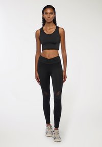 Czarny sportowy crop top i legginsy o wysokim stanie charakteryzują się gładką teksturą, geometrycznymi wstawkami z siateczki oraz dopasowanym krojem dla wygody.