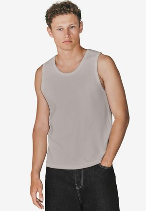 Világosszürke, ujjatlan pamut tanktop, körkivágással és laza szabással, sötét farmerrel párosítva. Sima textura, hétköznapi dizájn.