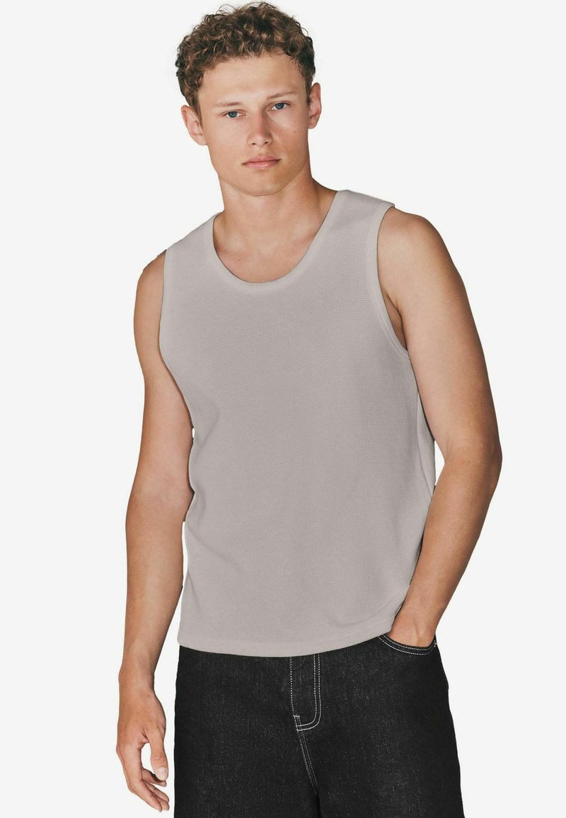 Jasnoszary, bezrękawnikowy T-shirt z bawełny, z okrągłym dekoltem i luźnym krojem, w zestawieniu z ciemnymi dżinsami. Gładka tekstura, swobodny design.