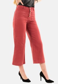 Pantaloni rossi a vita alta, croppati, con chiusura a cinque bottoni e due tasche posteriori. Tessuto liscio con una trama leggermente strutturata.