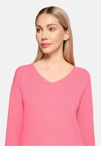 Pull en maille côtelée rose avec un col en V et des manches longues, doté d'une texture douce et d'un design ajusté.