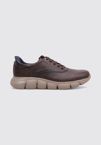 Zapatilla de cuero marrón con suela beige acolchada, forma redondeada, cordones planos y un acento azul marino en el cuello.