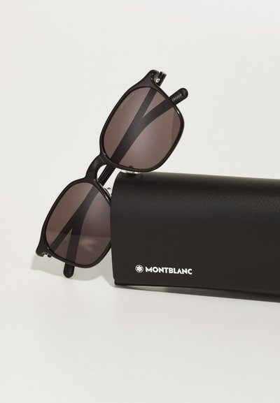Sorte solbriller med rektangulær form og brune tonede linser, hviler på et sortetui med en hvid "Montblanc"-logo.