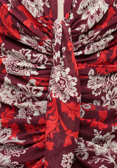 Tecido cor de vinho com padrões florais brancos e vermelhos, apresentando textura franzida e um detalhe de laço ao centro.