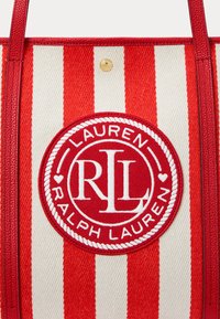 Tote torba z rdečimi in belimi črtami z tkano teksturo, ki ima kroglo izvezenega logotipa z napisom "Ralph Lauren" in inicialkami "RL".