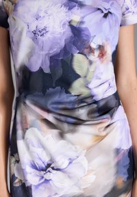 Robe à motifs floraux avec de grandes fleurs violettes et crèmes sur un fond sombre. Le matériau semble léger et a une texture lisse.