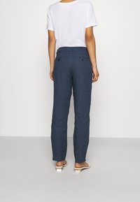 Pantalon en lin bleu avec une coupe droite, taille élastique et deux poches arrière, porté avec un t-shirt blanc uni et des sandales.