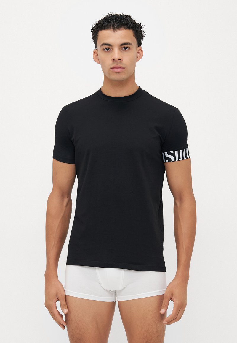 Schwarzes Kurzarm-T-Shirt aus Baumwolle mit Rundhalsausschnitt und einem markanten gemusterten Akzent am linken Ärmel.