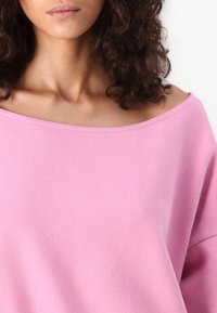Top rosa scollato con una texture morbida e una vestibilità ampia. Presenta un ampio scollo e dettagli di cucitura sottili.